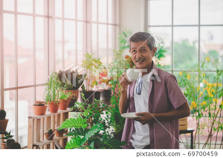Happy senior retired man having coffee in a greenhouse garden in Happy senior retired man having coffee in a greenhouse garden in 69700459