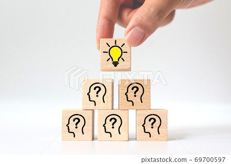 Hand picked wooden cube block with light bulb icon on top pyramid and head human symbol 69700597