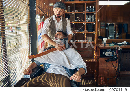 Fashionable hairdresser shaving his customer with an axe Fashionable hairdresser shaving his customer with an axe 69701149