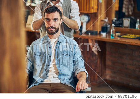 Brunette man looking serious during hair styling Brunette man looking serious during hair styling 69701190