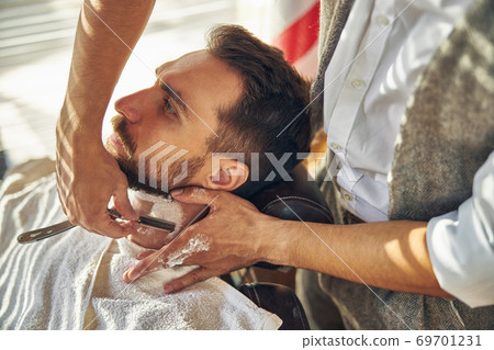 Brunette man having his neck shaved by a barber Brunette man having his neck shaved by a barber 69701231