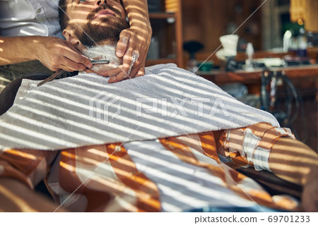 Brunette man in a checked shirt getting shaved Brunette man in a checked shirt getting shaved 69701233