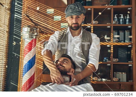 Serious barber shaving his client at a barbershop 69701234