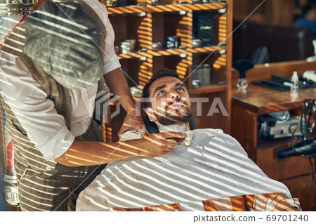 Brunette bearded man getting a shave at a hair salon 69701240
