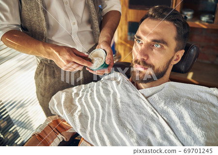 Professional hairdresser holding shaving cream and a brush Professional hairdresser holding shaving cream and a brush 69701245