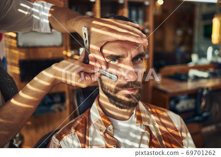 Serious young man having his beard groomed at a barbershop 69701262