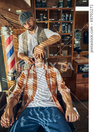 Professional hair-cutter turning head of his client ot the side to shave him Professional hair-cutter turning head of his client ot the side to shave him 69701271