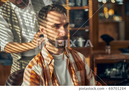 Serious barbershop client waiting for his barber to cut his hair Serious barbershop client waiting for his barber to cut his hair 69701284