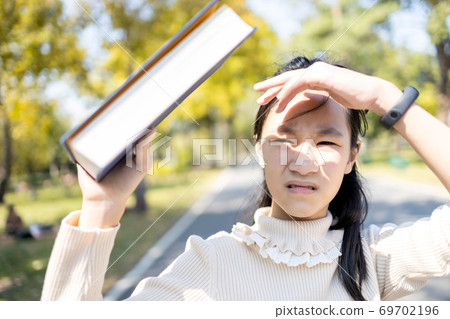 Asian child girl walking outdoor protects from the sunlight UV rays with her book,female teenager worried about hot strong sunburn,heat causes of melasma,wrinkles on the face and skin cancer,protectio 69702196