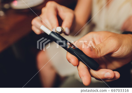 heat-not-burn tobacco product technology. Two woman e-cigarette in his hand before smoking. heat-not-burn tobacco product technology. Two woman e-cigarette in his hand before smoking. 69703316