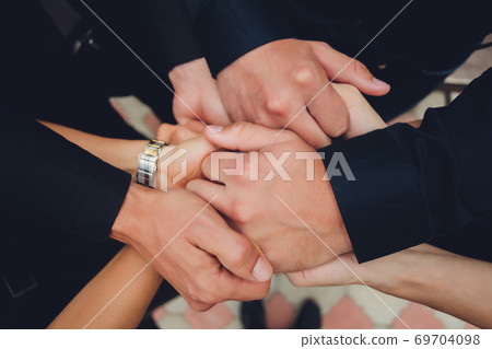 two man and three women holding hands on a table implying a polyamory relationship or love triangle. 69704098