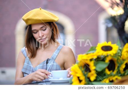 Woman drinking coffee in a cafe on the street. there is a bouquet of sunflowers on the table 69706250