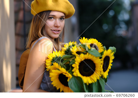 woman is walking in the old town. He is holding a bouquet of autumn sunflowers in his hand woman is walking in the old town. He is holding a bouquet of autumn sunflowers in his hand 69706260