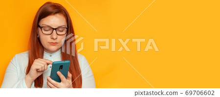 Business woman uses a smartphone, standing on a yellow background wall Business woman uses a smartphone, standing on a yellow background wall 69706602