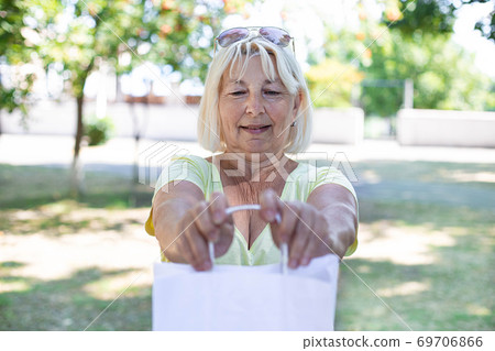 Adult blond woman with white paper bag standing on the street Adult blond woman with white paper bag standing on the street 69706866