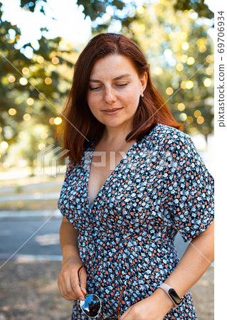 Portrait of a beautiful red-haired girl in a dress posing in a park on a sunny day 69706934