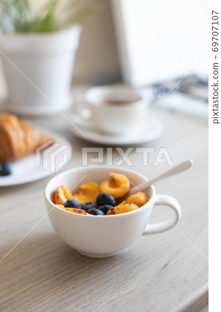 Delicious milk oatmeal with apricots and blueberries in a white bowl on a wooden table in the kitchen. Vertical photo Delicious milk oatmeal with apricots and blueberries in a white bowl on a wooden table in the kitchen. Vertical photo 69707107