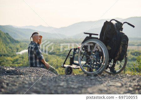 Sportsman after injury in wheelchair enjoy fresh air in the mountains. Nature therapy of people with disabilities. 69710055