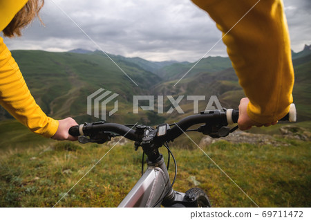Close-up of female hands holding handlebars of mountain bike outdoors on green grass background 69711472