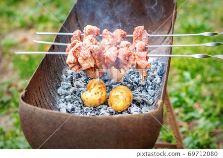 Man prepares barbecue meat with potatoes Man prepares barbecue meat with potatoes 69712080