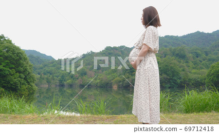 Profile of a pregnant woman standing by the pond Profile of a pregnant woman standing by the pond 69712418