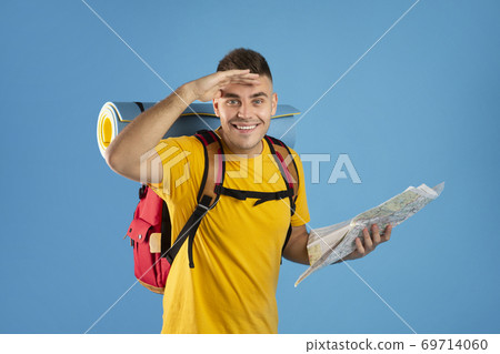 Happy millennial tourist with camping equipment and map looking at camera on blue studio background 69714060