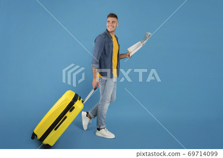 Full length portrait of positive young guy with luggage and map walking on blue studio background, copy space 69714099