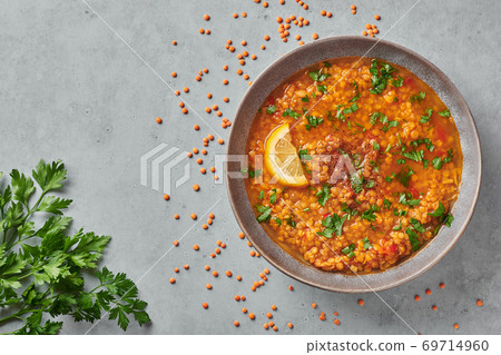 Red lentils tomato soup with parsley and lemon in gray plate on concrete table top. Vegetarian dish. 69714960