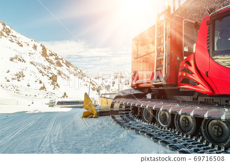 Red modern snowcat ratrack with snowplow snow grooming machine preparing ski slope piste hill at alpine skiing winter resort Ischgl in Austria. Heavy machinery mountain equipment track vehicle 69716508
