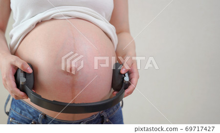A young mom wearing headphones to listen to prenatal care A young mom wearing headphones to listen to prenatal care 69717427