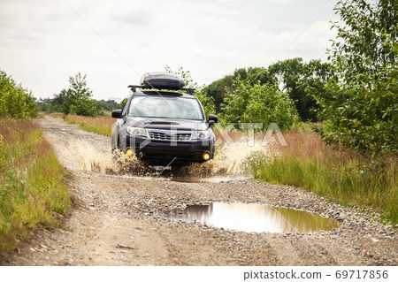 Black Subaru Forester driving on a  dirt road with puddles. 69717856