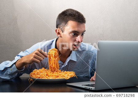 man eating spaghetti with tomato sauce and watching the computer man eating spaghetti with tomato sauce and watching the computer 69718298