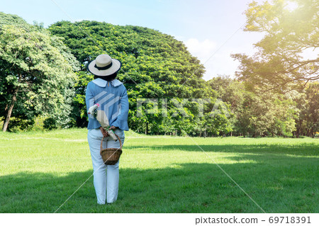 Elderly lifestyle concept. Back of senior women 50s with hat while holding fruit basket and bouquet 69718391