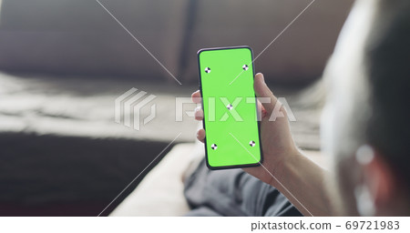 man holding smartphone with green screen while relaxing on couch 69721983