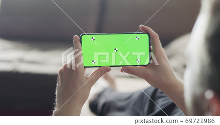 man holding smartphone with green screen while relaxing on couch man holding smartphone with green screen while relaxing on couch 69721986