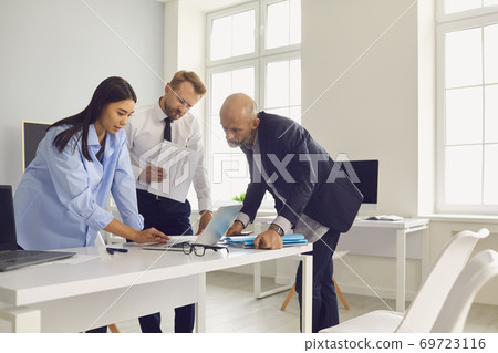 Business team looking at laptop screen analyzing research data while working on project together Business team looking at laptop screen analyzing research data while working on project together 69723116
