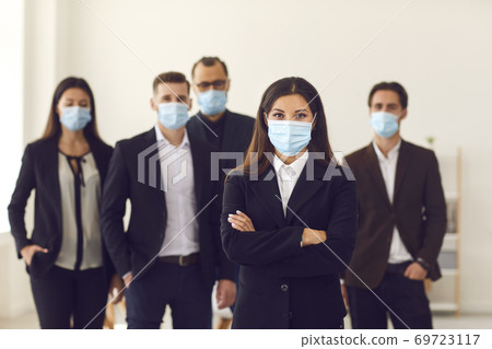 Responsible young company manager with group of workers all wearing face masks at work Responsible young company manager with group of workers all wearing face masks at work 69723117