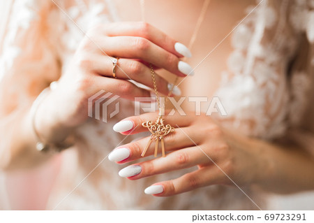 Beautiful luxury bride in elegant white dress holds golden necklace in the hands 69723291