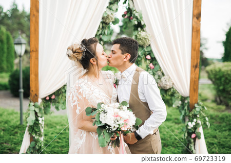 Beautiful bride and groom embracing and kissing on their wedding day outdoors 69723319