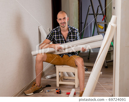 A man is smiling sitting on a bench with rolls of Wallpaper in his hands. A man is smiling sitting on a bench with rolls of Wallpaper in his hands. 69724091