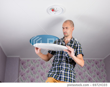 A happy man on a stepladder is going to install an led ceiling light. 69724103