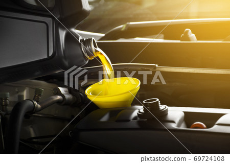 Mechanic pouring engine oil to car engine in garage shop 69724108