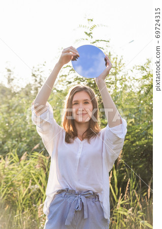 Authentic caucasian girl smiling and holds a small round mirror Authentic caucasian girl smiling and holds a small round mirror 69724315