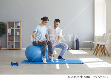Man doctor chiropractor fixing woman on fitness ball in right position for pain relief 69724887