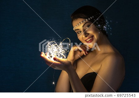 Christmas portrait of a young brunette girl holding a glowing ball made of LED lights in her hands. Christmas portrait of a young brunette girl holding a glowing ball made of LED lights in her hands. 69725543