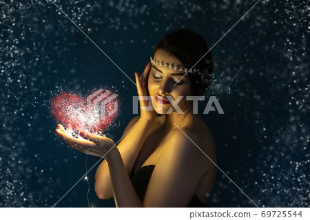 Christmas portrait of a young brunette girl holding a glowing ball made of LED lights in her hands. Christmas portrait of a young brunette girl holding a glowing ball made of LED lights in her hands. 69725544