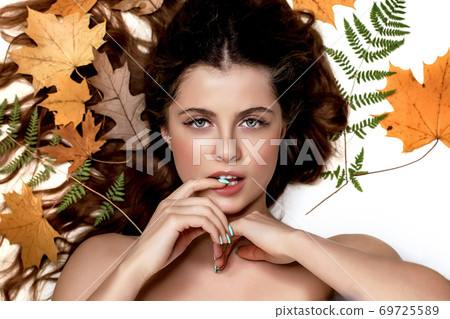 Portrait of a young brunette woman on a white background with a green fern and yellow leaves around her head Portrait of a young brunette woman on a white background with a green fern and yellow leaves around her head 69725589