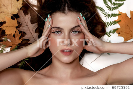 Portrait of a young brunette woman on a white background with a green fern and yellow leaves around her head 69725591