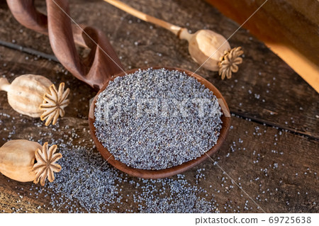 Poppy seeds on a spoon with poppy pods in the background 69725638