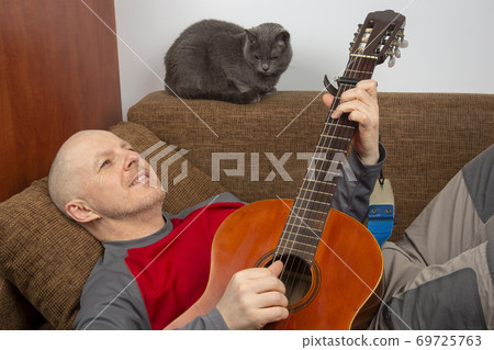 man in at home in quarantine because of an epidemic of coronavirus plays a classical guitar  69725763